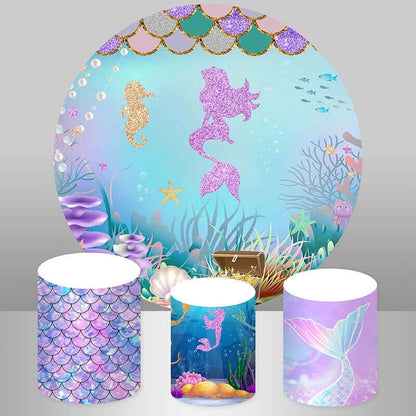 Mermaid princess glitter-themed party decor set featuring a round backdrop with a pink glitter mermaid silhouette, seahorse, treasure chest, and coral reef, paired with three cylinder covers showcasing a pastel scale design, underwater scene, and mermaid tail graphic.