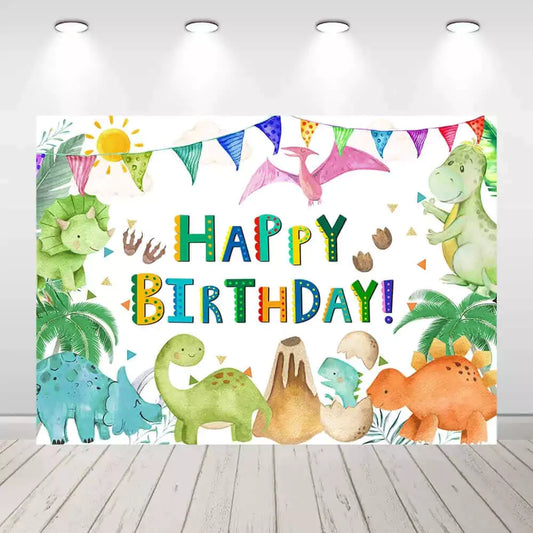 A colorful dinosaur-themed birthday party backdrop featuring cartoon baby dinosaurs, a volcano, dinosaur eggs, palm trees, and multicolored 'Happy Birthday!' text.