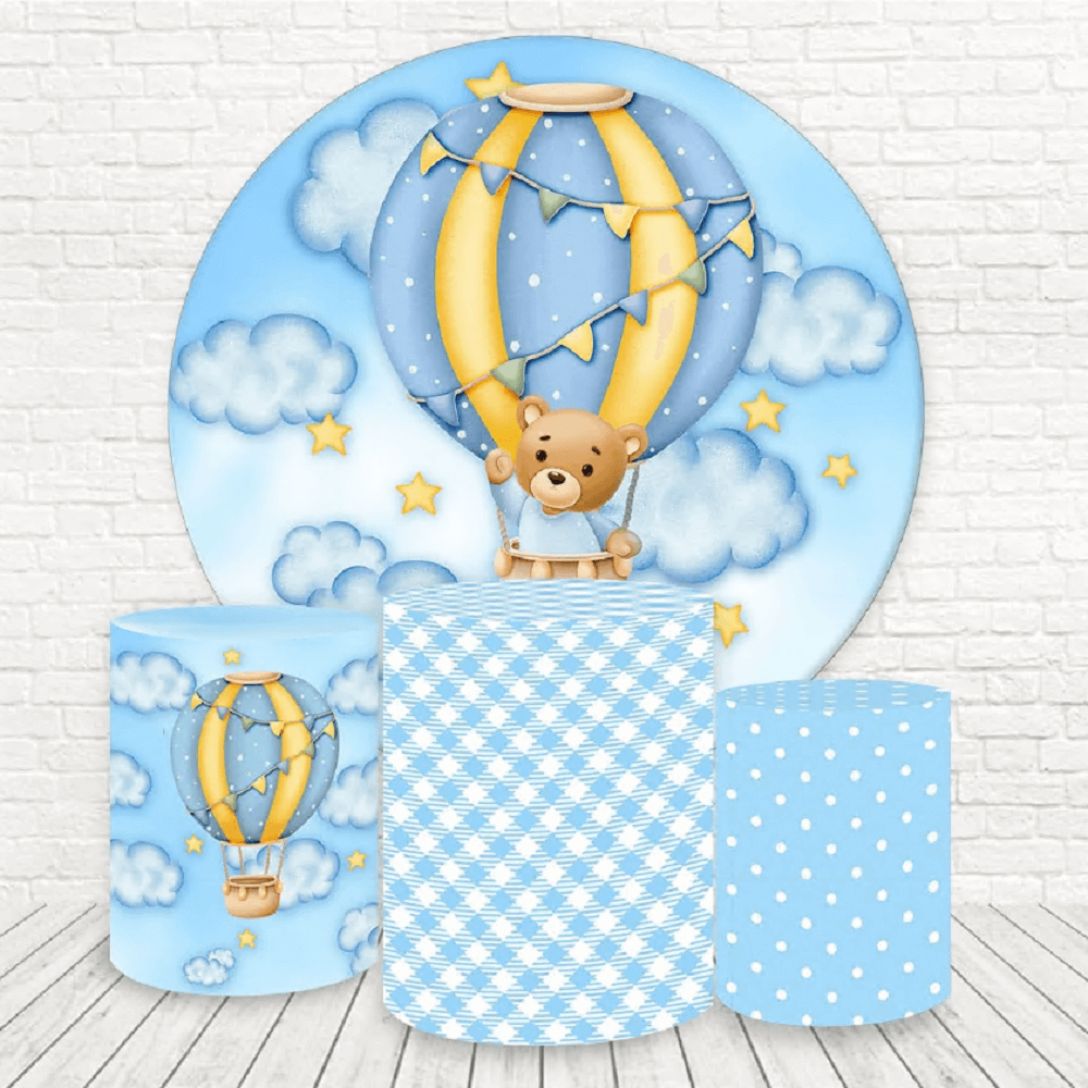 A hot air balloon-themed party decor set featuring a circular backdrop with a teddy bear in a blue and yellow hot air balloon among clouds and stars, and three cylinder covers with hot air balloons, gingham, and polka dot designs.