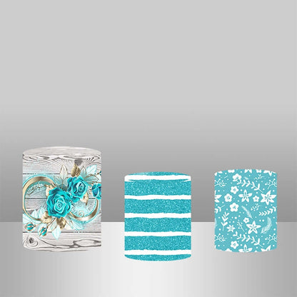 A set of three decorative cylinder covers with coordinated designs: one featuring a blue floral motif, another with glittery blue stripes, and a third with a playful blue and white floral print.