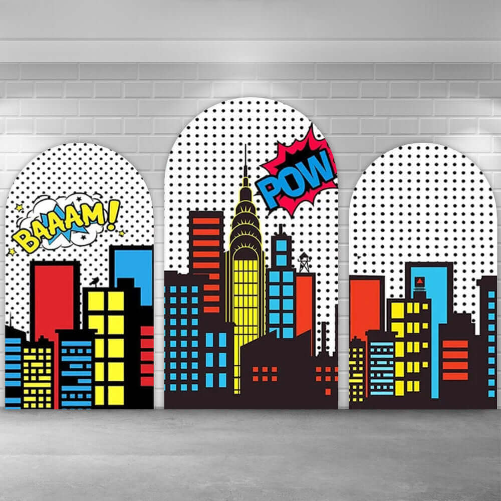 Three-piece cartoon cityscape arch backdrop featuring vibrant red, yellow, and blue buildings with comic captions “BAAAM!” and “POW!” on a black-and-white polka-dot background.