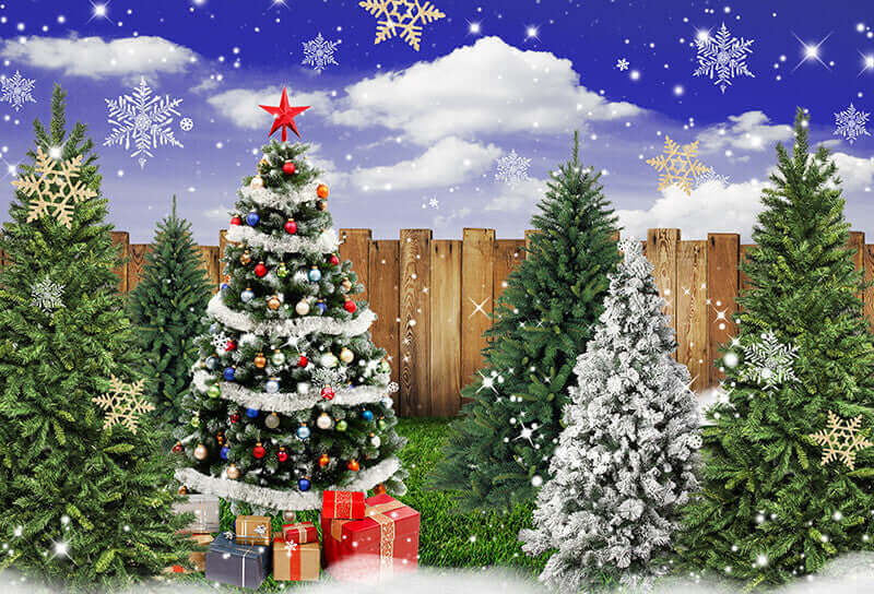 Christmas photography backdrop with a snowy Christmas tree, wooden fence, snowflakes, and gift boxes under a clear winter sky.