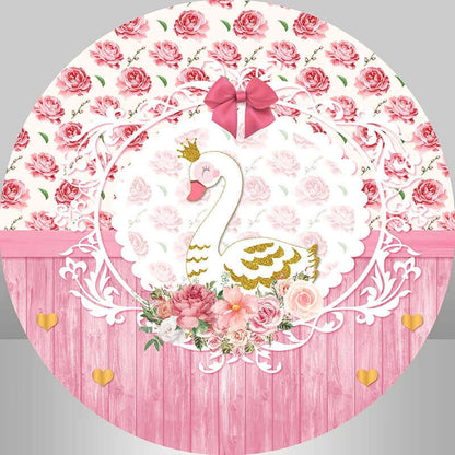 Round pink backdrop with a golden crowned swan in a floral arrangement, set against a pink wood background with golden hearts and roses.