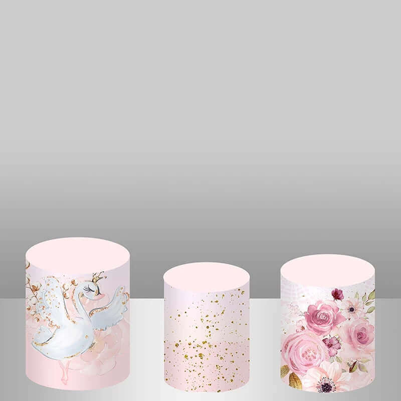 Set of three plinth covers for swan-themed party decor: one with swans and florals, one with gold splatter on pink, and one with lush pink floral arrangements.