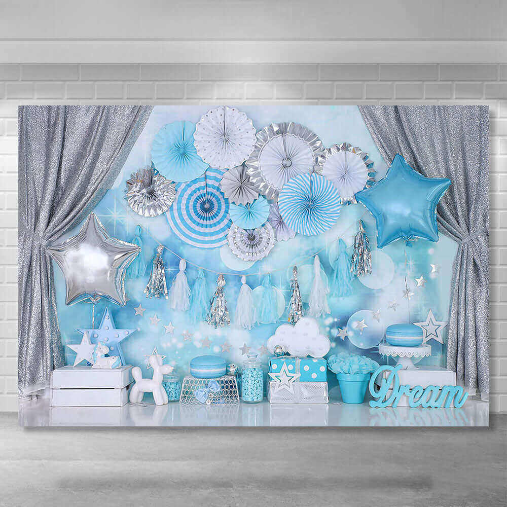 Dream-themed children’s birthday party backdrop with glitter silver curtains, blue star balloons, paper fans, tassel garlands, and star and cloud decorations, perfect for elegant celebrations.