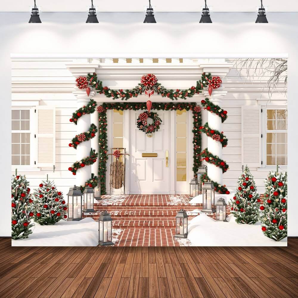 Elegant Christmas porch backdrop featuring a white house with garlands wrapped around pillars, a wreath on the door, snow-covered trees, and festive red and gold decorations.