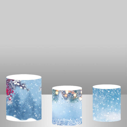 Three winter-themed cylinder covers featuring designs of snow-covered branches with red berries, evergreen branches with glowing holiday lights, and a frosty snowy background with a soft blue tone.