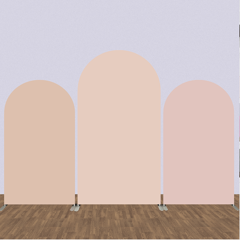 Set of three solid color arched backdrops in soft nude tones of peach, blush pink, and beige, placed on a wooden floor, ideal for minimalist event decor.