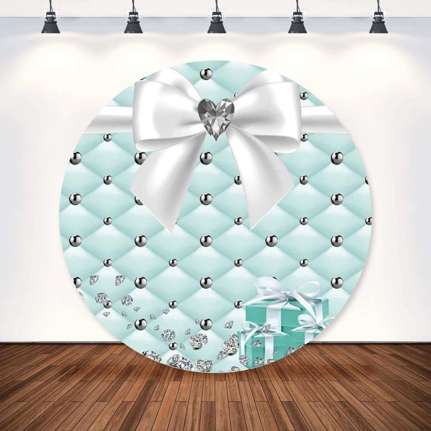 Round party backdrop featuring a Tiffany-blue quilted design adorned with silver diamond embellishments, a white bow with a heart-shaped diamond, and elegant gift box accents.