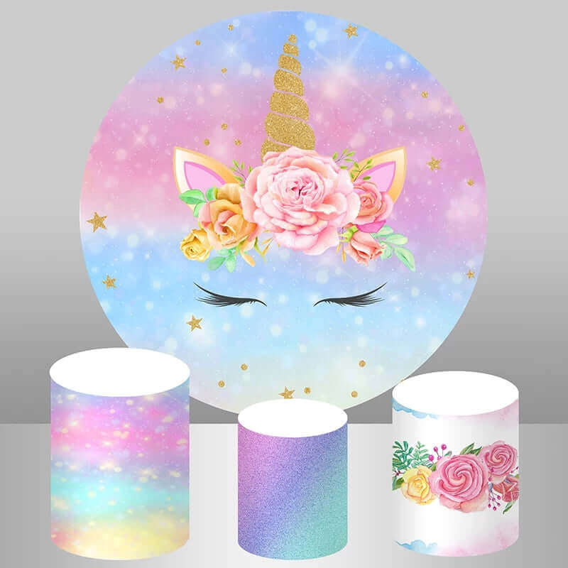 Unicorn-themed party decor set featuring a round pastel rainbow backdrop with a glittering golden unicorn horn, floral accents, and three cylinder covers with rainbow glitter, pastel hues, and floral patterns.