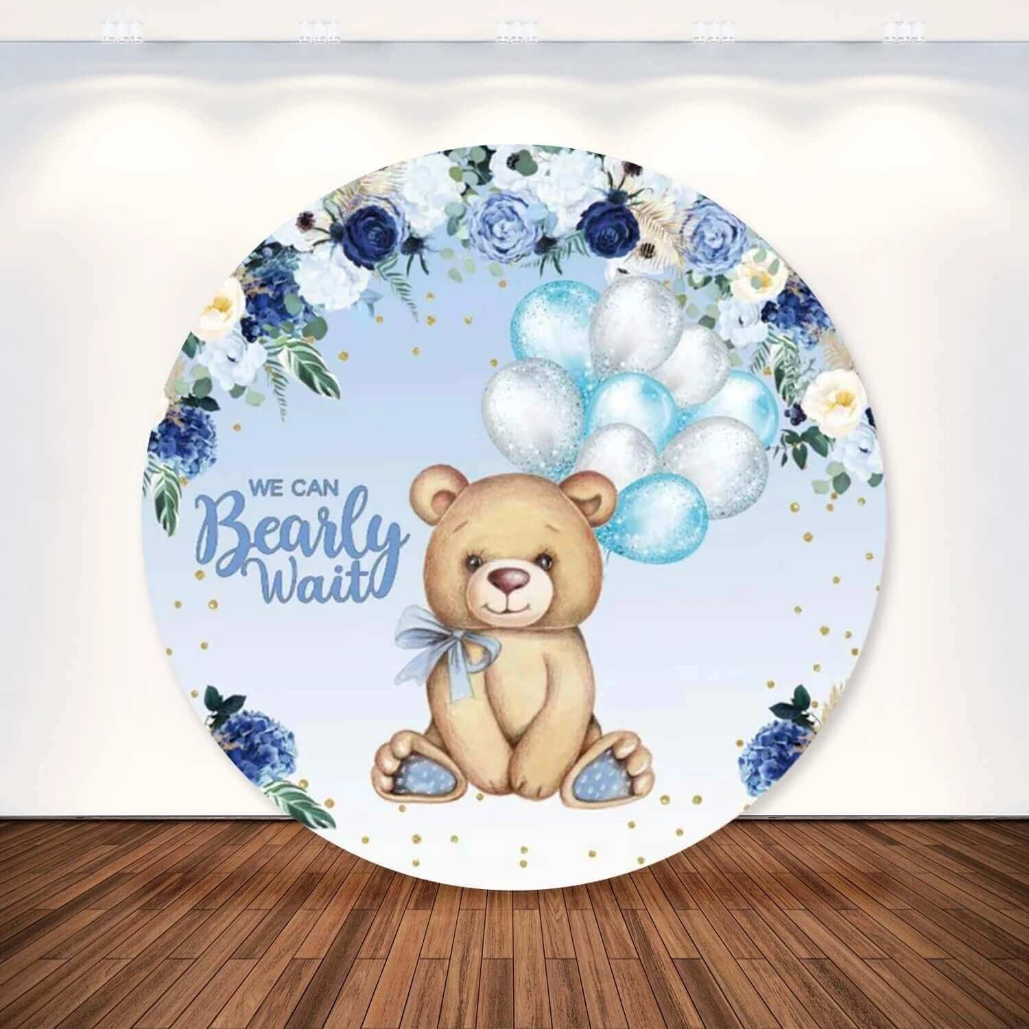 Round party backdrop featuring a teddy bear with blue and silver balloons, surrounded by blue and white floral arrangements, perfect for baby showers or gender reveal events.